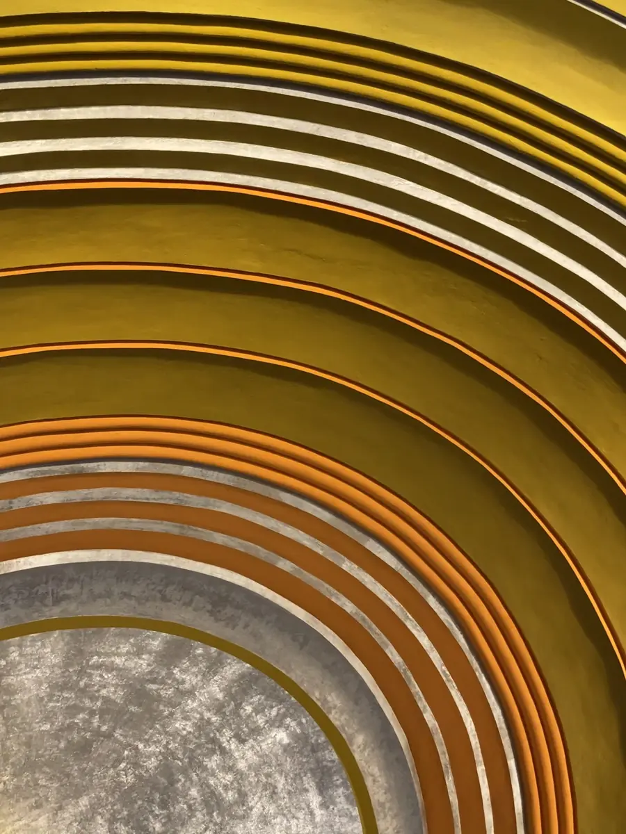 A tall photo looking up at the same ceiling, with the golden rings curving around a textured silver-gray center at the bottom