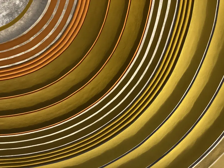 A photo looking up at a curved ceiling of concentric rings in mustard yellow, orange and silver, with soft shadows along each ridge